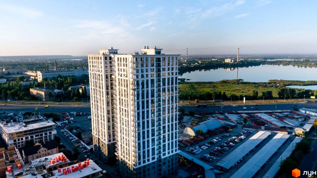 Вид на висотний житловий комплекс Метрополія з білою фасадною обробкою та численними вікнами. Навколо комплексу розташовані паркувальні місця та будівельні майданчики.