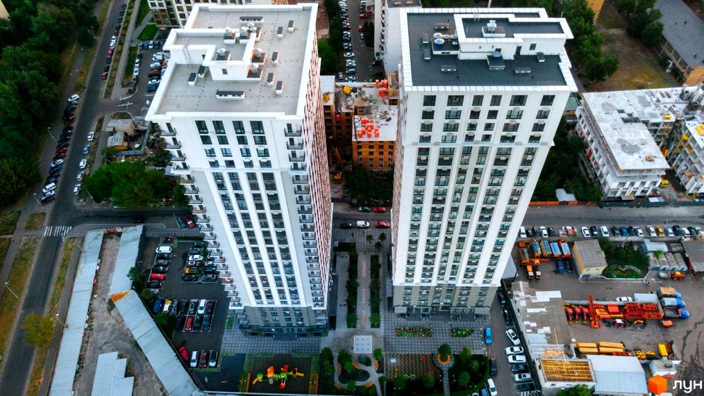 Вид на житловий комплекс Метрополія з висоти пташиного польоту. Два висотних будинки з білими фасадами та численними вікнами, між ними зелені зони та паркувальні місця.