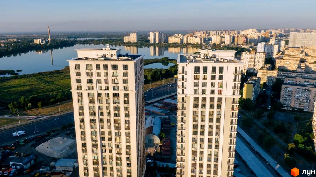 Зовнішній вигляд житлового комплексу Метрополія з двома висотними будинками, що виходять на місто та водойму. Навколо комплексу розташована міська інфраструктура та зелені насадження.