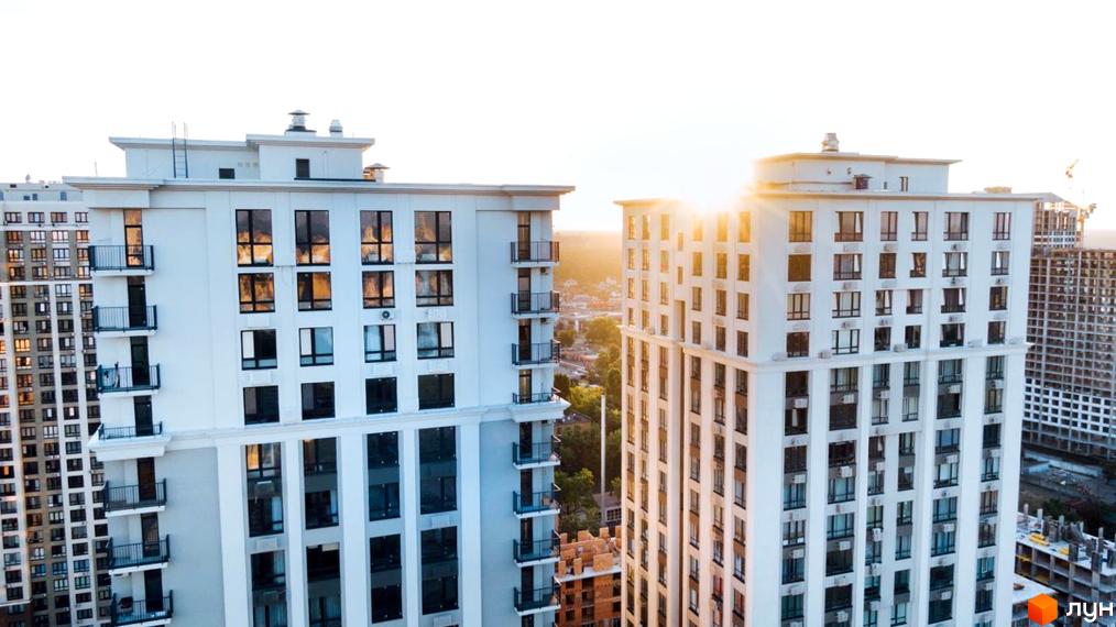 Сучасний житловий комплекс Метрополія з білими фасадами та великою кількістю вікон. Навколо видно інші новобудови та будівельні майданчики.