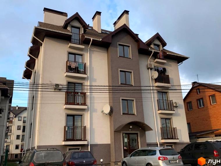 Зовнішній вигляд житлового комплексу Петрівський: багатоповерховий будинок зі світлими фасадами та коричневими дахами. На балконах сушиться білизна. Біля будинку припарковані автомобілі.