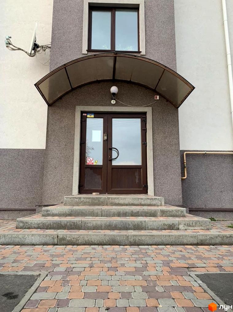 Вхідна група житлового комплексу Петрівський з навісом, дверима та сходами. Прибудинкова територія викладена плиткою.