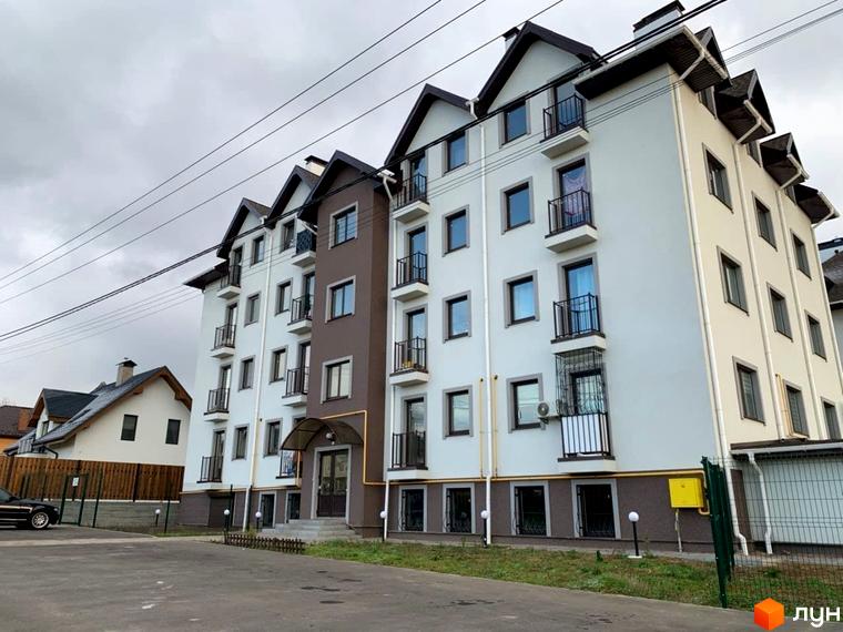 Новобудова ЖК Петрівський з біло-коричневим фасадом та балконами. Навколо будинку розташована прибудинкова територія з деревами та парковкою.