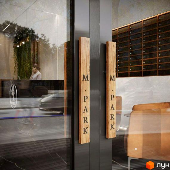 Вхід до Житлового комплексу M.Park з прозорими скляними дверима та дерев'яними ручками. У фокусі видно рецепцію та поштові скриньки.