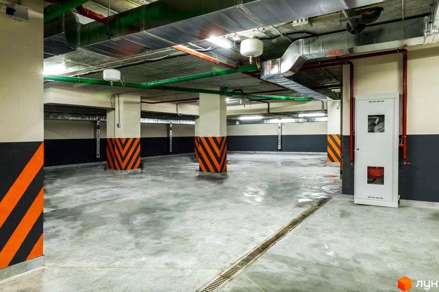 Фото паркінгу в ЖК Схід. Підземний паркінг з пофарбованими колонами та системою вентиляції.