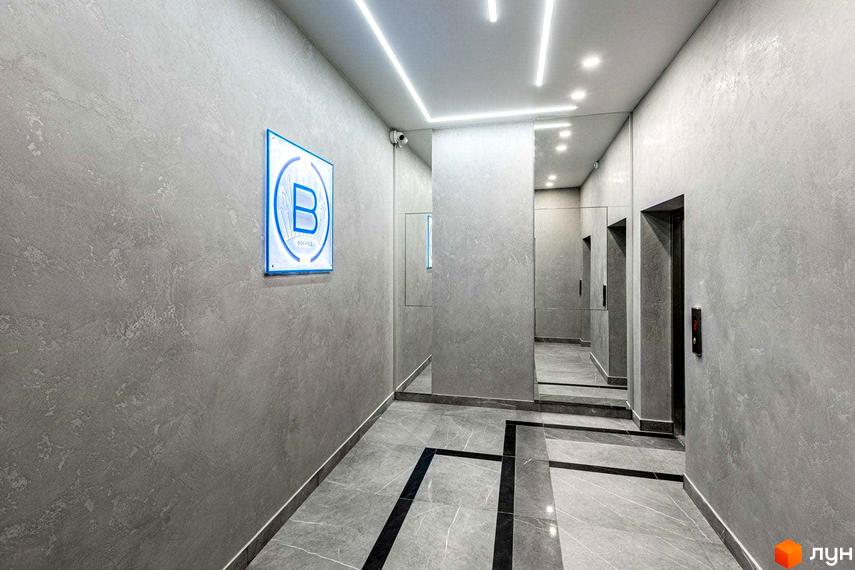 Інтер'єр холу житлового комплексу Схід, що відображає загальний дизайн будинку: сірі стіни, плитка на підлозі, яскраве освітлення.