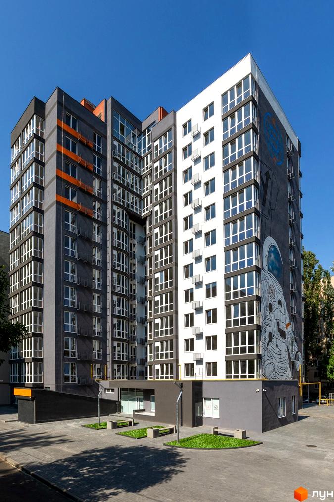 Житловий комплекс Схід з сіро-білим фасадом, помаранчевими акцентами та муралом космонавта. Прибудинкова територія з бруківкою та зеленими насадженнями.