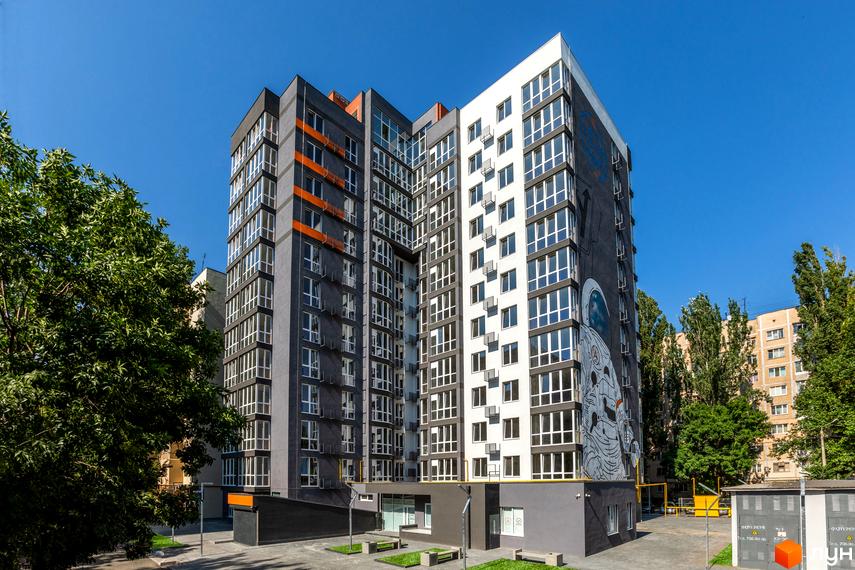 Житловий комплекс Схід: багатоповерховий будинок з сіро-білим фасадом та муралом. Прибудинкова територія з деревами та лавками.