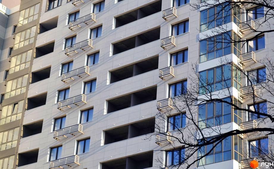 Фасад житлового комплексу Островського, 40 з балконами та великими вікнами. Прибудинкова територія з деревами на передньому плані.