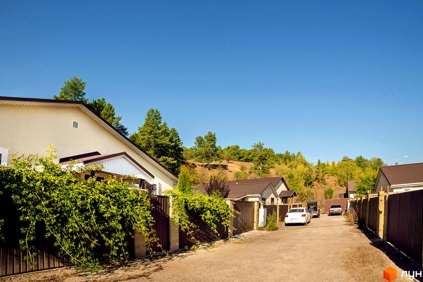 Котеджне містечко Лисичкина діброва. Будинки з коричневими дахами та світлими стінами розташовані вздовж вулиці з зеленими насадженнями та парканом.