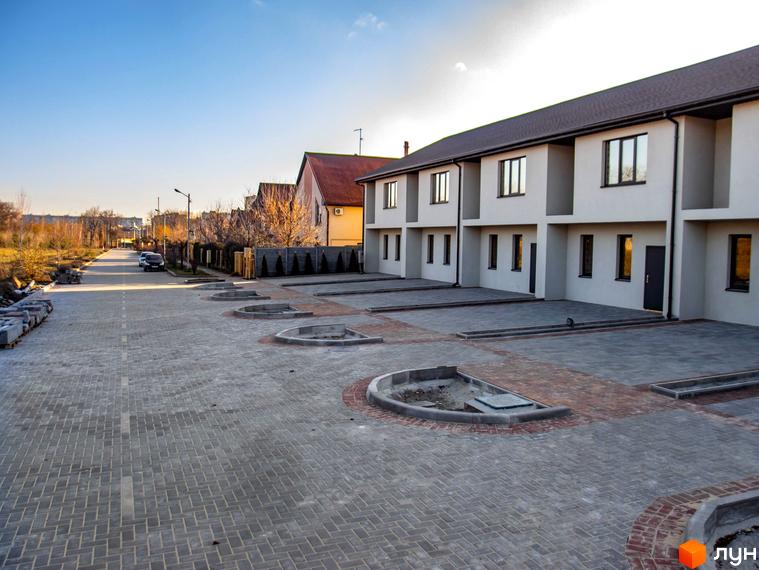 Ряд світлих будівель Комплексу таунхаусів „Європейський“ з темними дахами та вікнами, перед якими вимощені бруківкою подвір'я та дорога.
