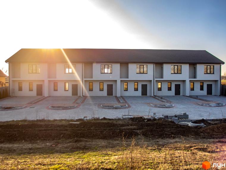 Таунхаус „Європейський“: ряд двоповерхових таунхаусів світлого кольору з темними дахами. Перед будинками вимощена територія, на передньому плані видно ґрунт.