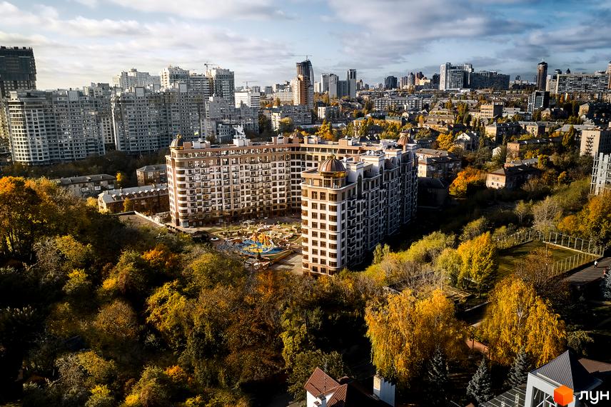 Житловий комплекс 52 Перлина (Pechersk Plaza) з великою кількістю вікон та куполоподібними дахами. На прибудинковій території розташований дитячий майданчик, навколо будинку багато дерев.