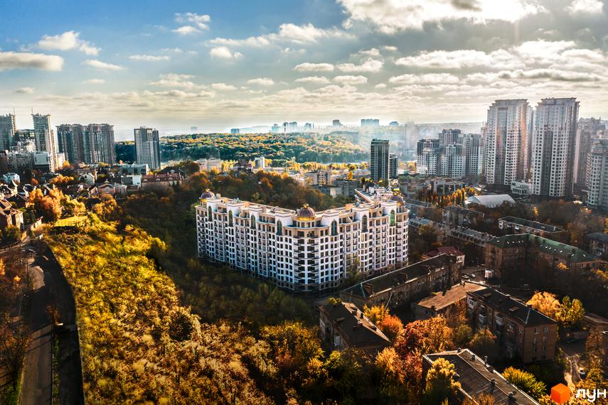 Житловий комплекс 52 Перлина (Pechersk Plaza) з білими фасадами на фоні осіннього пейзажу. Навколо будинку розташовані дерева та інші будівлі.