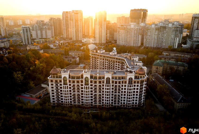 Житловий комплекс Pechersk Plaza з фасадом у світлих тонах на тлі міської забудови. На даху будівлі розташовані декоративні елементи, а навколо - зелені насадження.