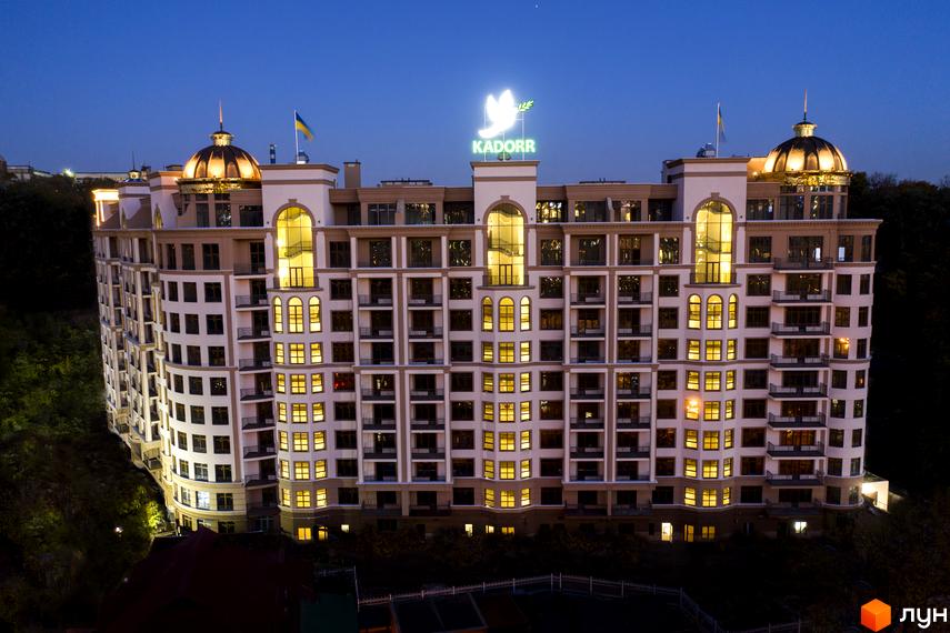 Висотна будівля ЖК Kadorr з великою кількістю вікон, балконів та куполоподібними дахами. На даху будівлі розташований логотип компанії та український прапор.