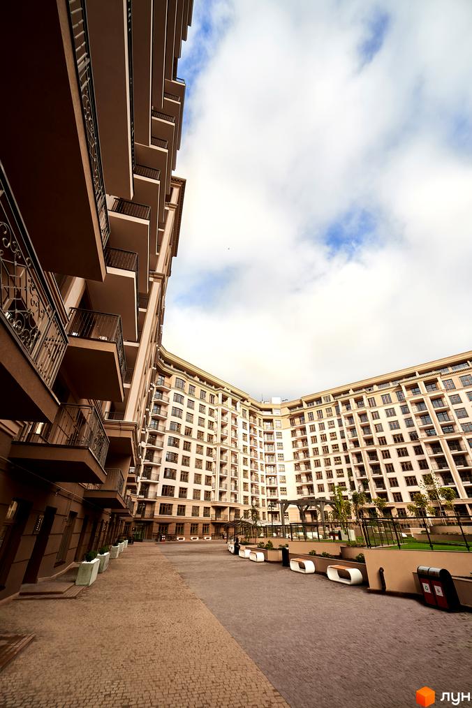 Зображення фасаду багатоповерхового будинку ЖК 52 Перлина (Pechersk Plaza). На території комплексу розташовані лавки та декоративні елементи.