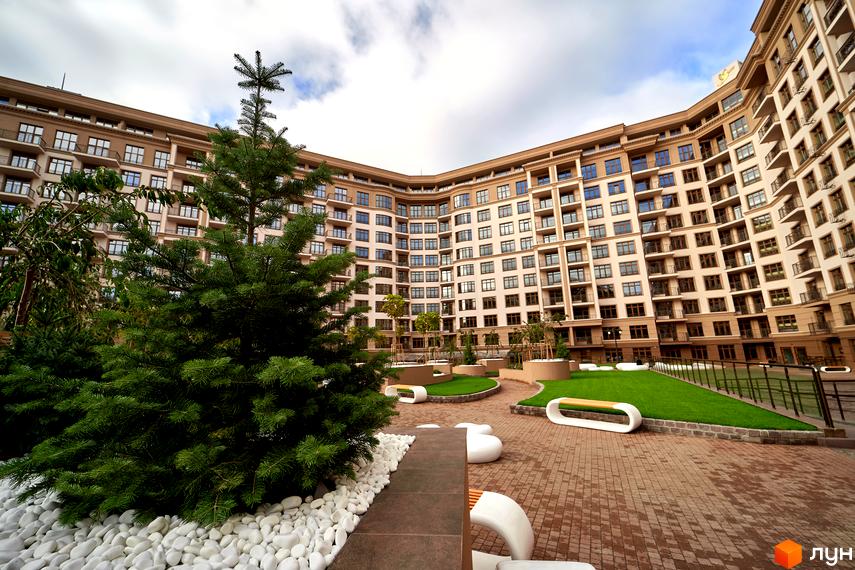 Житловий комплекс 52 Перлина (Pechersk Plaza). Багатоповерховий будинок з великою кількістю вікон та балконів. На прибудинковій території розташовані газони, лавки та декоративні елементи.