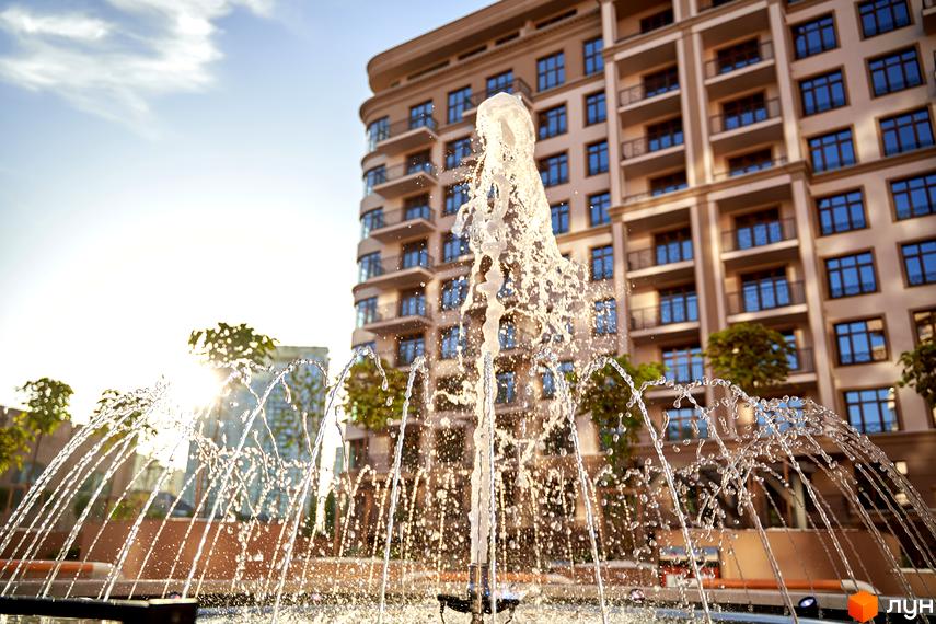 Житловий комплекс 52 Перлина (Pechersk Plaza). Фасад будівлі з великими вікнами та балконами. На передньому плані фонтан з водою.