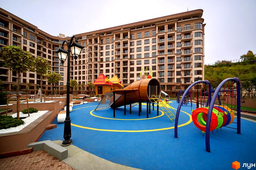 Житловий комплекс 52 Перлина (Pechersk Plaza) з дитячим майданчиком на території. Висотна будівля з великою кількістю вікон, поруч зона відпочинку з гойдалками.