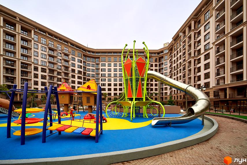 Житловий комплекс 52 Перлина (Pechersk Plaza). Високі будинки з великою кількістю вікон. На території дитячий майданчик з гіркою та гойдалками.