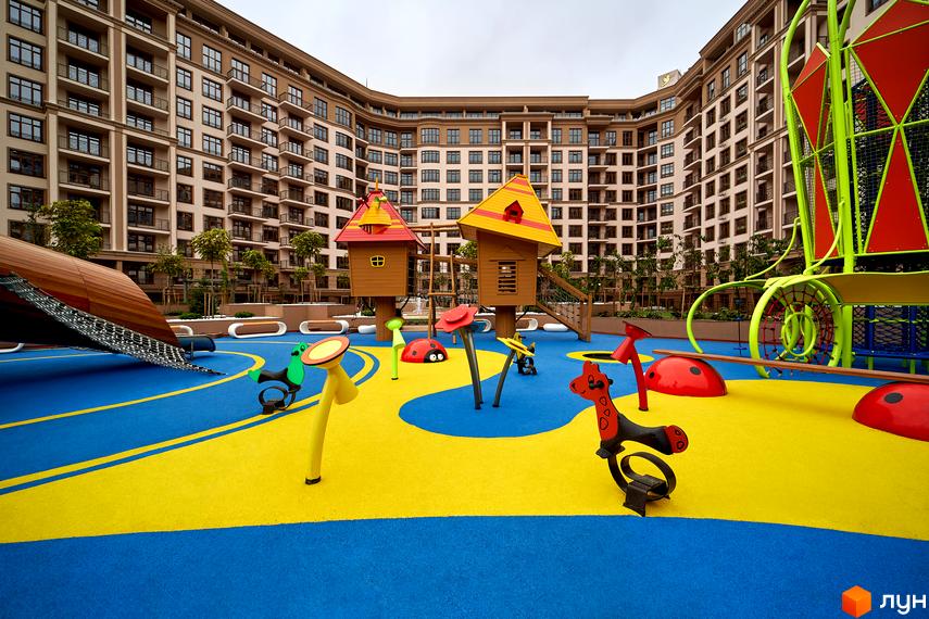 Житловий комплекс 52 Перлина (Pechersk Plaza) з дитячим майданчиком. Вид на будівлю з великою кількістю вікон та прибудинкову територію з яскравим дитячим обладнанням.