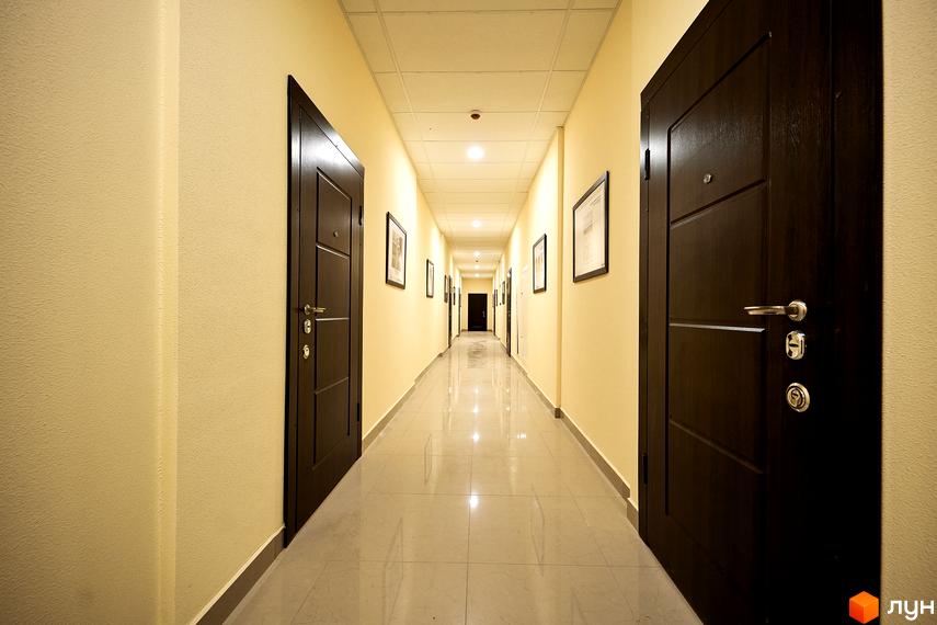 Коридор в ЖК 52 Перлина (Pechersk Plaza) з дверима та картинами на стінах. Світло відбивається від глянцевої підлоги.