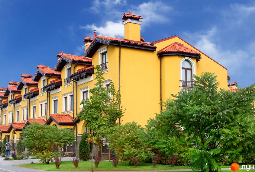 Котеджне містечко КМ Італійський квартал з жовтими фасадами та червоними дахами. Поруч зелені дерева та кущі.