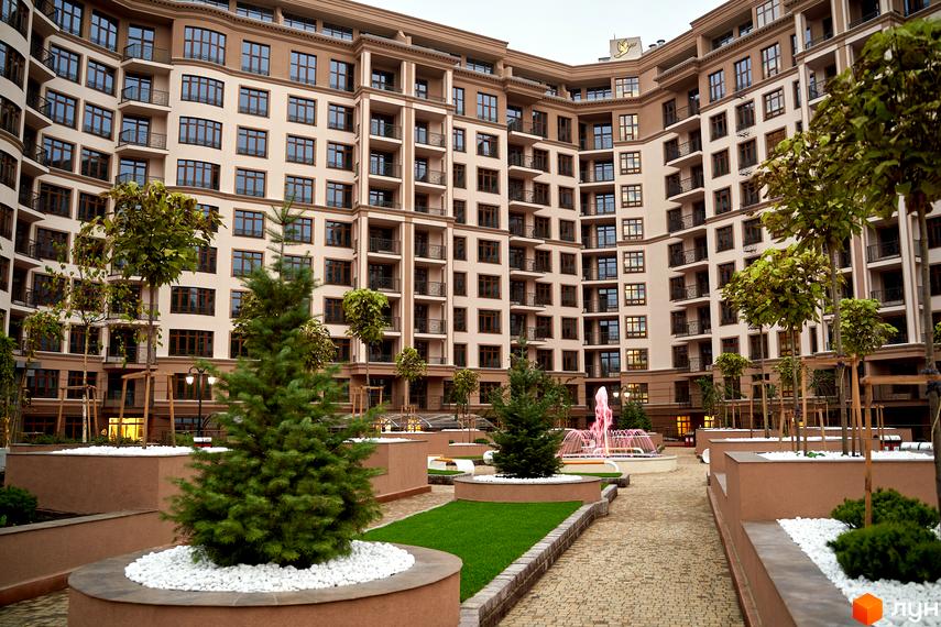 Житловий комплекс 52 Перлина (Pechersk Plaza). Висотна будівля з численними вікнами та балконами. На прибудинковій території розташовані дерева, зелені насадження та фонтан.