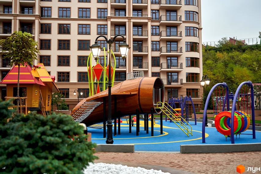 Житловий комплекс 52 Перлина (Pechersk Plaza). Висотна будівля з великою кількістю вікон. На території дитячий майданчик з гірками та гойдалками.