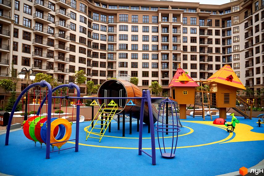 Житловий комплекс 52 Перлина (Pechersk Plaza). На фото зображено дитячий майданчик на фоні багатоповерхового будинку з балконами. На території є гойдалки, гірки та інші розваги для дітей.
