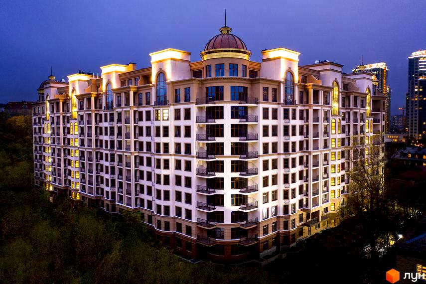 Житловий комплекс 52 Перлина (Pechersk Plaza) у вечірньому освітленні. Багатоповерховий будинок з великою кількістю вікон та балконів, розташований на фоні зелені.
