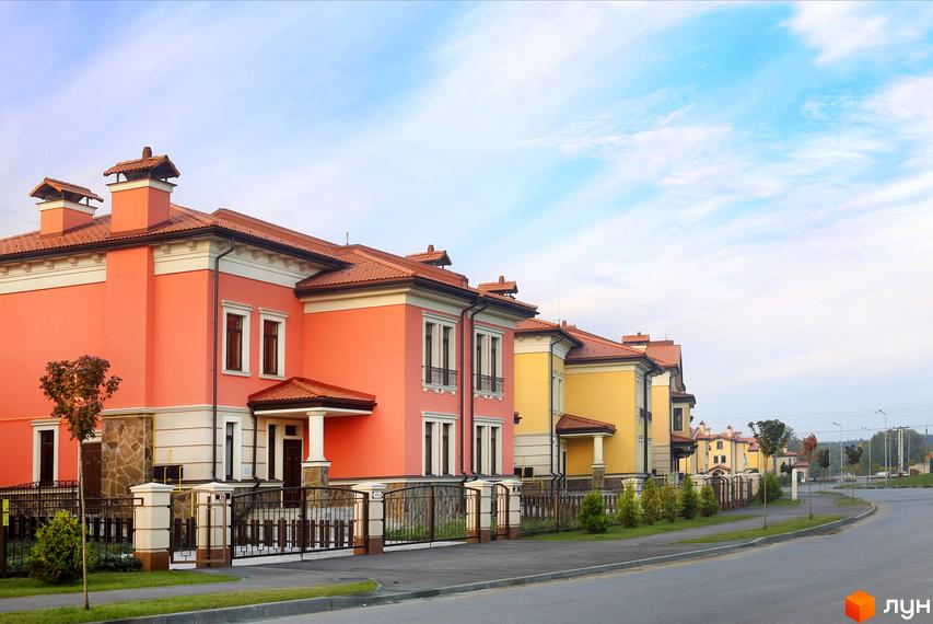 Котеджне містечко КМ Італійський квартал. Яскраві фасади будинків у жовтому та кораловому кольорах, доглянута прибудинкова територія з парканом та зеленими насадженнями.