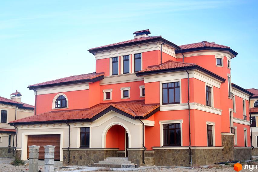 Котеджне містечко КМ Італійський квартал: двоповерховий будинок з червоною черепичною кришею та фасадом персикового кольору. Навколо будинку облаштована прибудинкова територія з елементами ландшафтного дизайну.