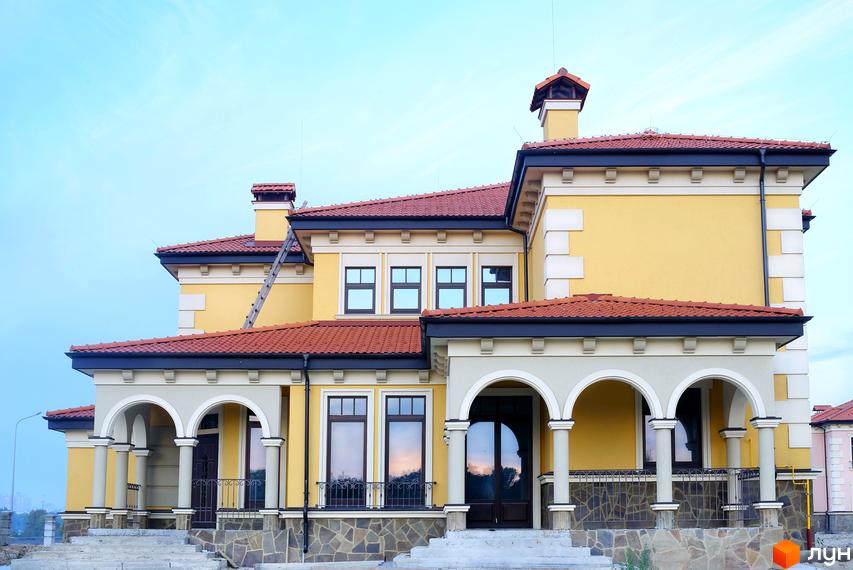 Котеджне містечко Італійський квартал: жовтий двоповерховий будинок з червоним черепичним дахом, арками та колонами. Навколо будинку облаштована прибудинкова територія.