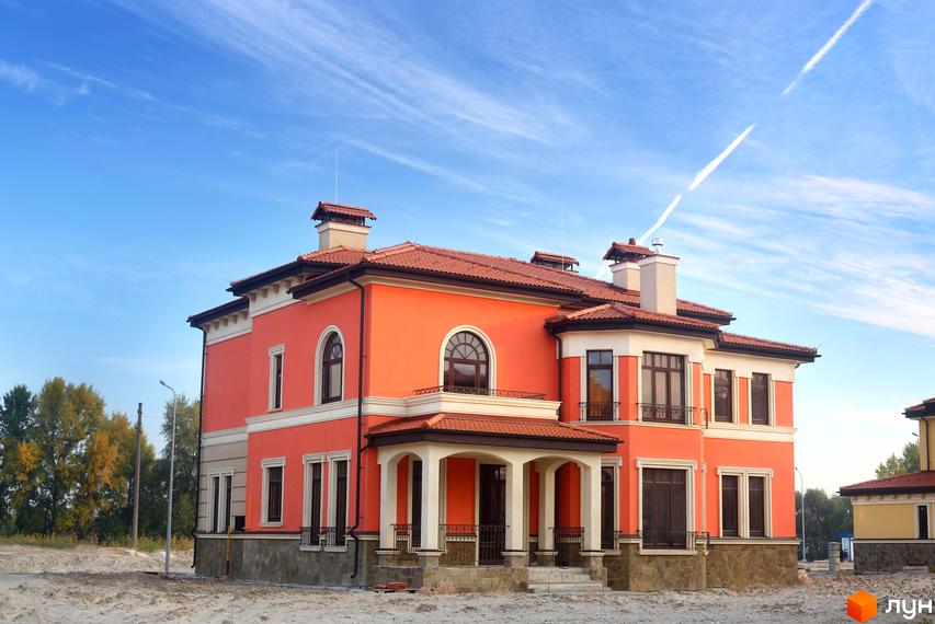 Котеджне містечко КМ Італійський квартал. Будинок з червоним черепичним дахом та помаранчевими стінами, розташований на піщаній ділянці з деревами на задньому плані.