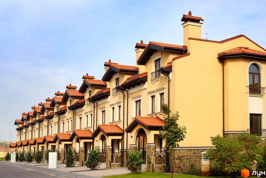 Котеджне містечко КМ Італійський квартал. Фасади двоповерхових будинків з червоними черепичними дахами та жовтими стінами, доглянута прибудинкова територія з зеленими насадженнями.