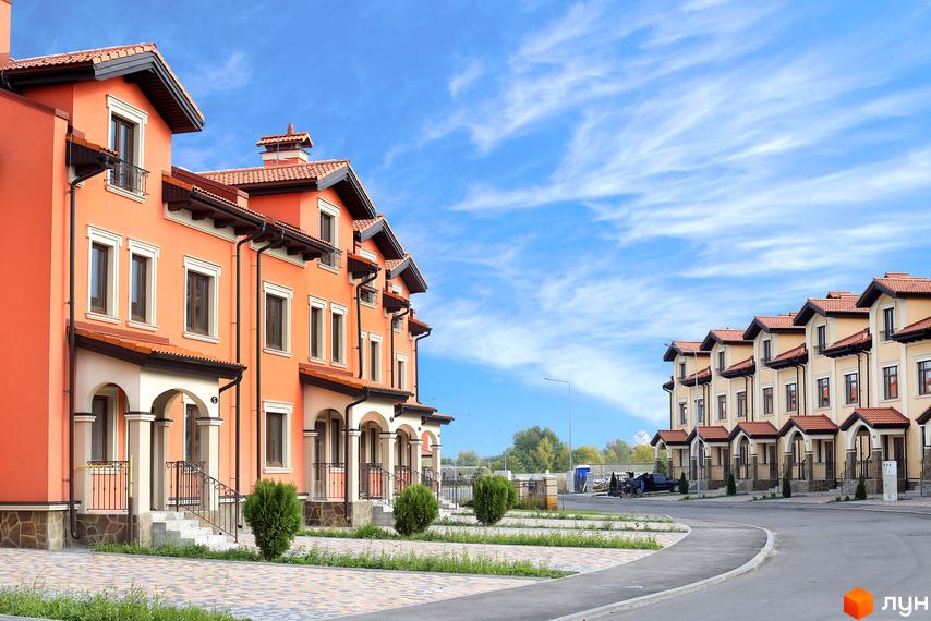 Котеджне містечко Італійський квартал з фасадами оранжевого та бежевого кольору. Охайний двір з доглянутими зеленими насадженнями та бруківкою.