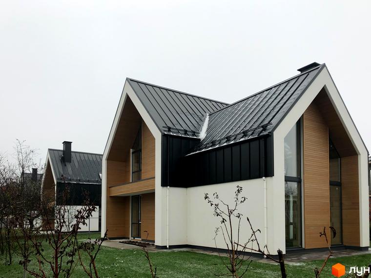 Котеджне містечко КМ Hill Park з сучасними фасадами та великими вікнами на фоні сірого неба. Навколо будівель зелений газон та дерева.