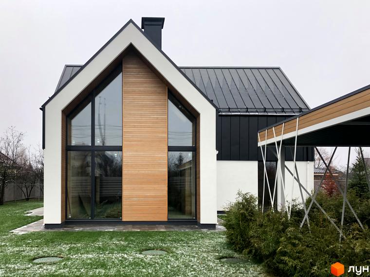 Котеджне містечко КМ Hill Park. Зовнішній вигляд будинку з панорамними вікнами та дерев'яним оздобленням фасаду, прибудинкова територія з газоном та кущами.