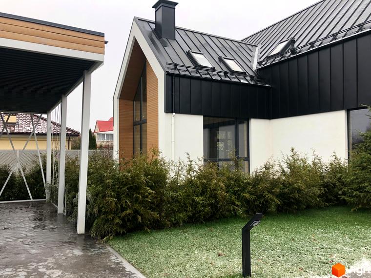 Котеджне містечко КМ Hill Park: фасад будинку з чорним металевим дахом та дерев'яними елементами, прибудинкова територія з ялинами та газоном.