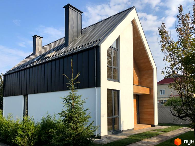 Котеджне містечко КМ Hill Park: двоповерховий будинок з чорним металевим дахом та білою штукатуркою, дерев'яними елементами та зеленими насадженнями навколо.