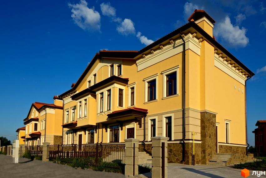 Котеджне містечко КМ Італійський квартал. Фасад будинку виконаний у жовтих тонах з кам'яним оздобленням цоколя. Огороджена територія з парканом та стовпчиками.
