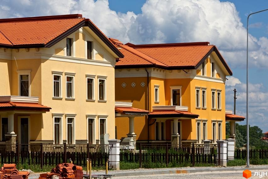 Котеджне містечко КМ Італійський квартал. Двоповерхові будинки жовтого кольору з червоними черепичними дахами, огороджена територія з парканом та зеленими насадженнями.
