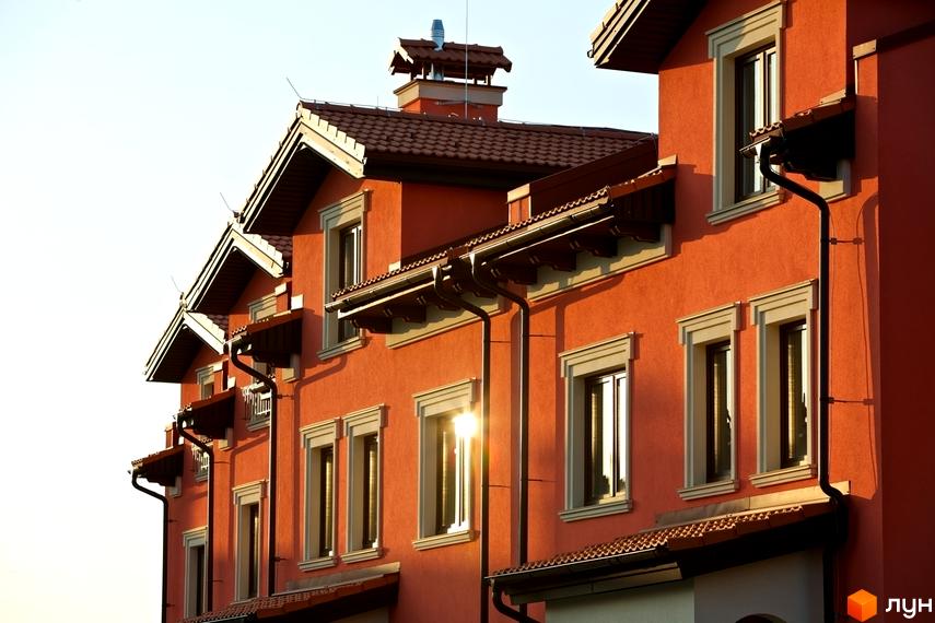 Котеджне містечко КМ Італійський квартал. Фасад будинку виконаний в помаранчевому кольорі з коричневими дахами та вікнами. Сонячні промені відбиваються у вікнах.