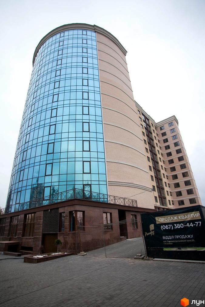 Фото фасаду Житлового комплексу Paradise з синіми вікнами та рекламою продажу квартир. Вигляд багатоповерхового будинку з вулиці.