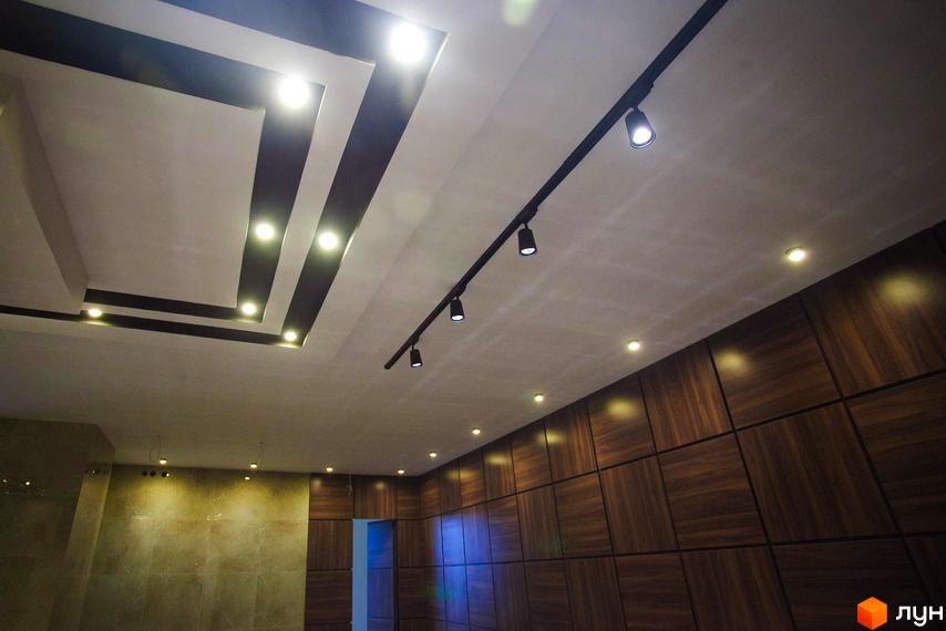 Інтер'єр приміщення з освітленням. Світлі стіни та дерев'яні панелі, точкові світильники на стелі. Фото для Житлового комплексу Paradise.