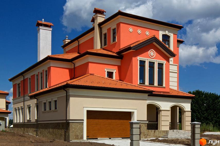 Котеджне містечко КМ Італійський квартал. Фасад будинку виконаний у помаранчевих та бежевих тонах, з черепичним дахом та кам'яною обробкою цоколя. Навколо будинку облаштована прибудинкова територія з елементами ландшафтного дизайну.