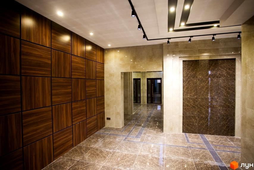 Інтер'єр вхідної зони Житлового комплексу Paradise з оздобленням стін дерев'яними та керамічними панелями. На підлозі плитка з імітацією мармуру.