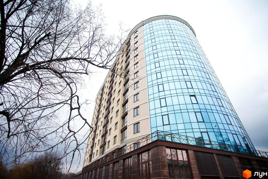 Багатоповерховий будинок Житлового комплексу Paradise з вигнутим скляним фасадом та світлими стінами. Поруч видно оголені гілки дерев на тлі сірого неба.